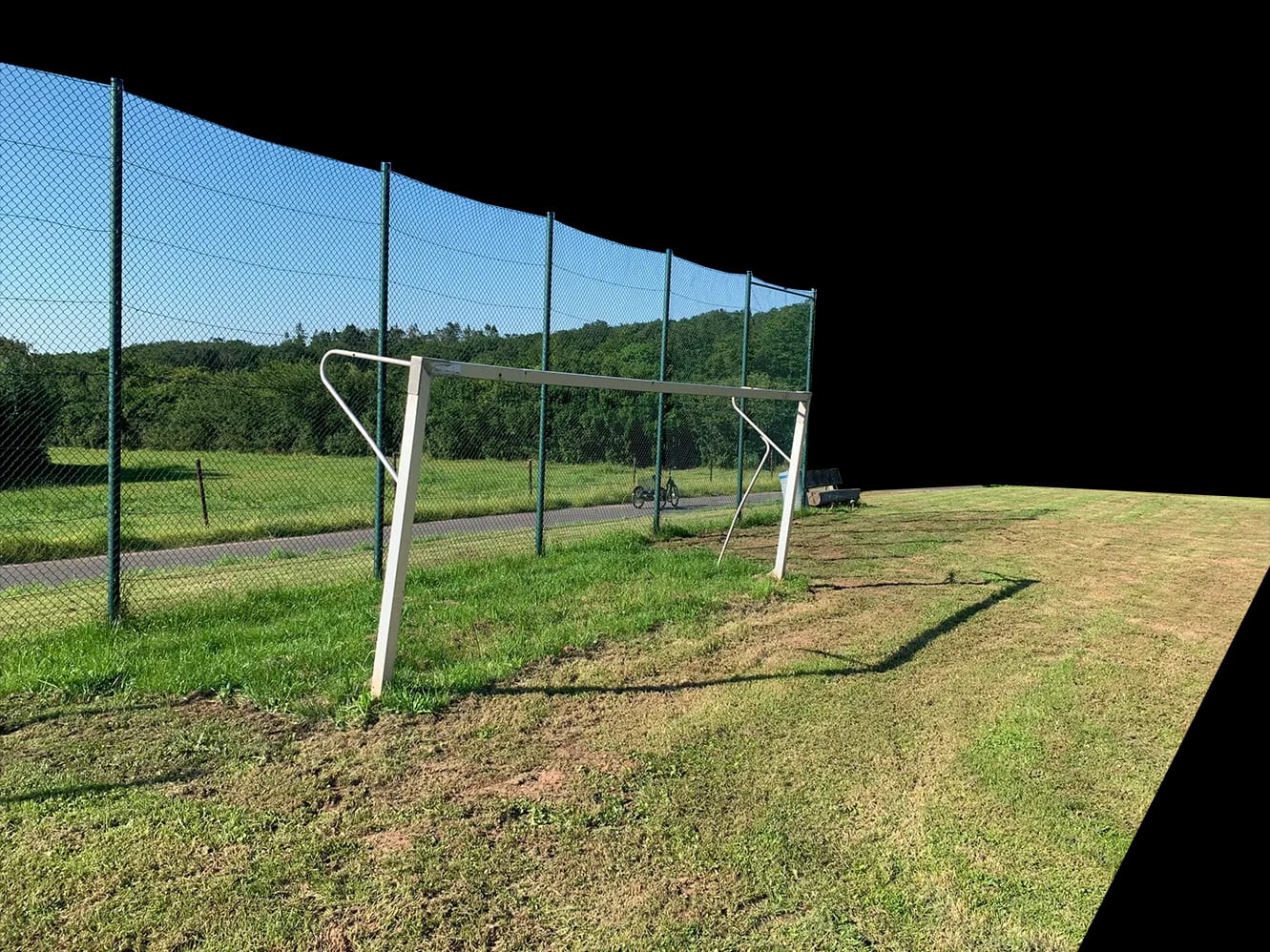 Ein Fußballtor vor dem hohen Gitterzaun, dahinter Bäume