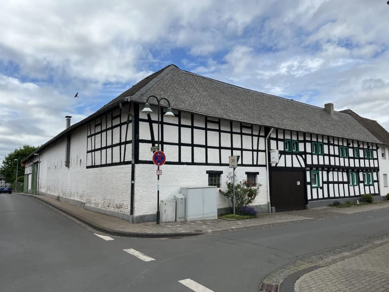 Langgestrecktes weißes Fachwerkhaus mit schwarzem Gebälk an einer Straßenecke