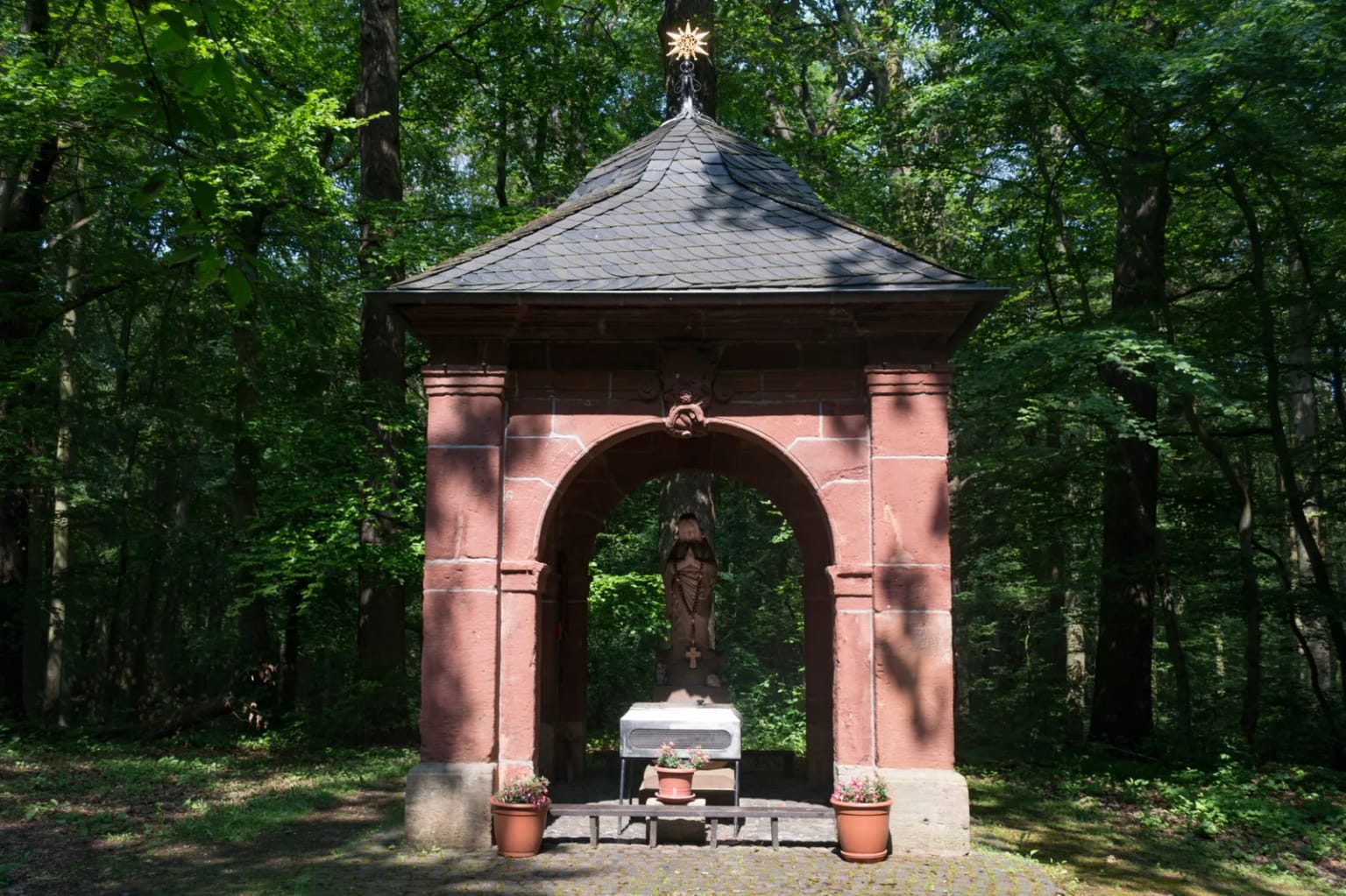 Die Waldkapelle im Eickser Busch, ein kleiner offener Bau aus rotem Sandstein zwischen hohen Bäumen