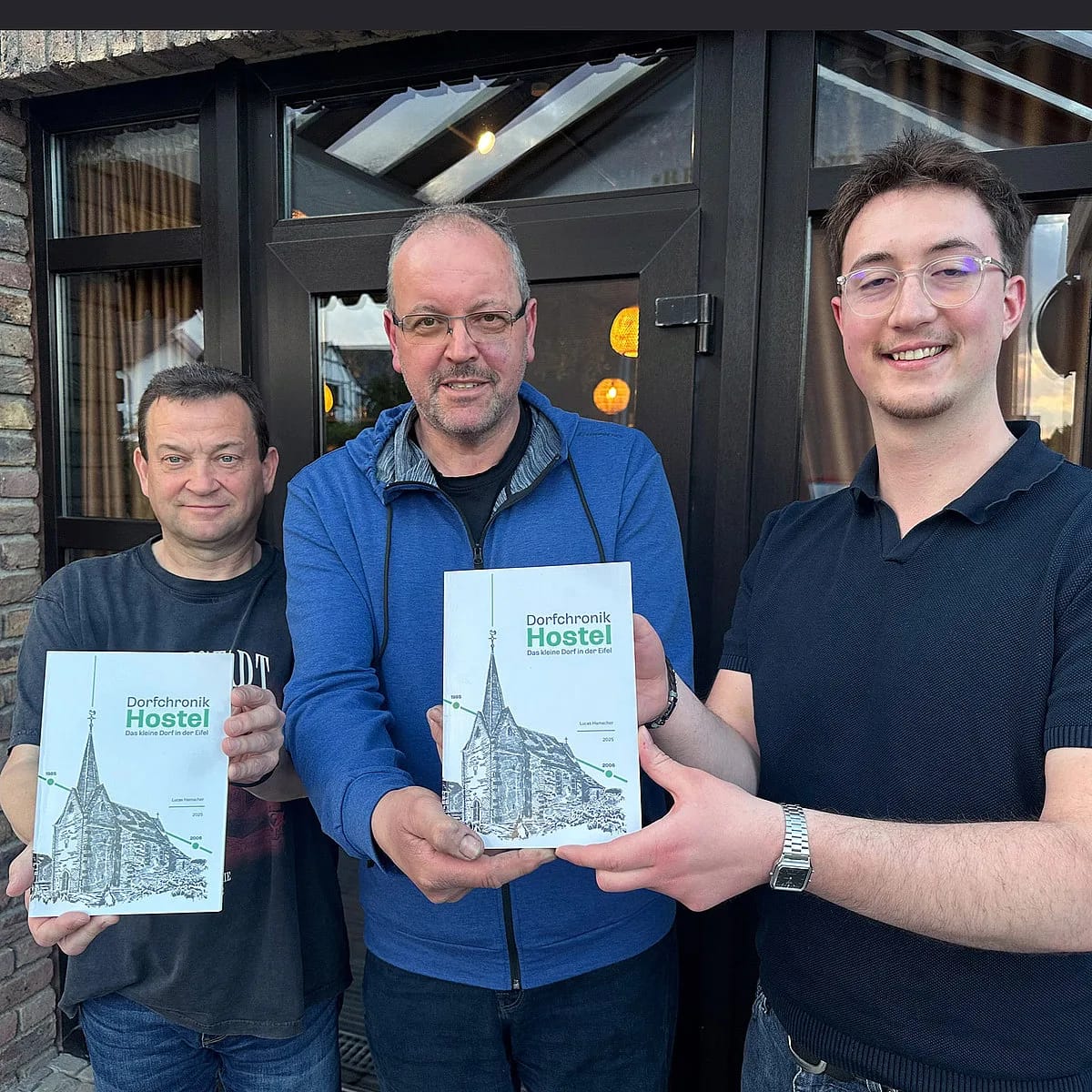 Drei Männer halten zwei Exemplare der Dorfchronik in die Kamera, rechts Lucas Hamacher